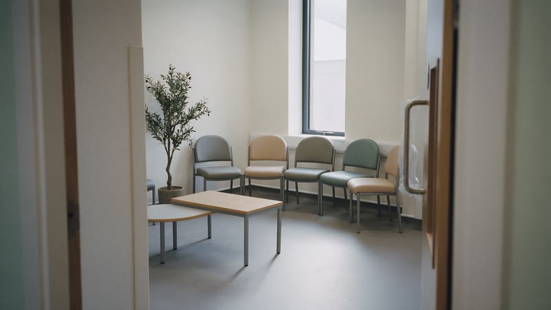 An empty waiting area in a newly finished clinic, with chairs along the wall, a low table and a potted tree.